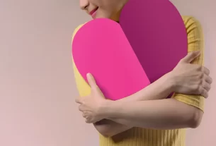 mulher alegre abraçada a um coração simbolizando a autoestima.