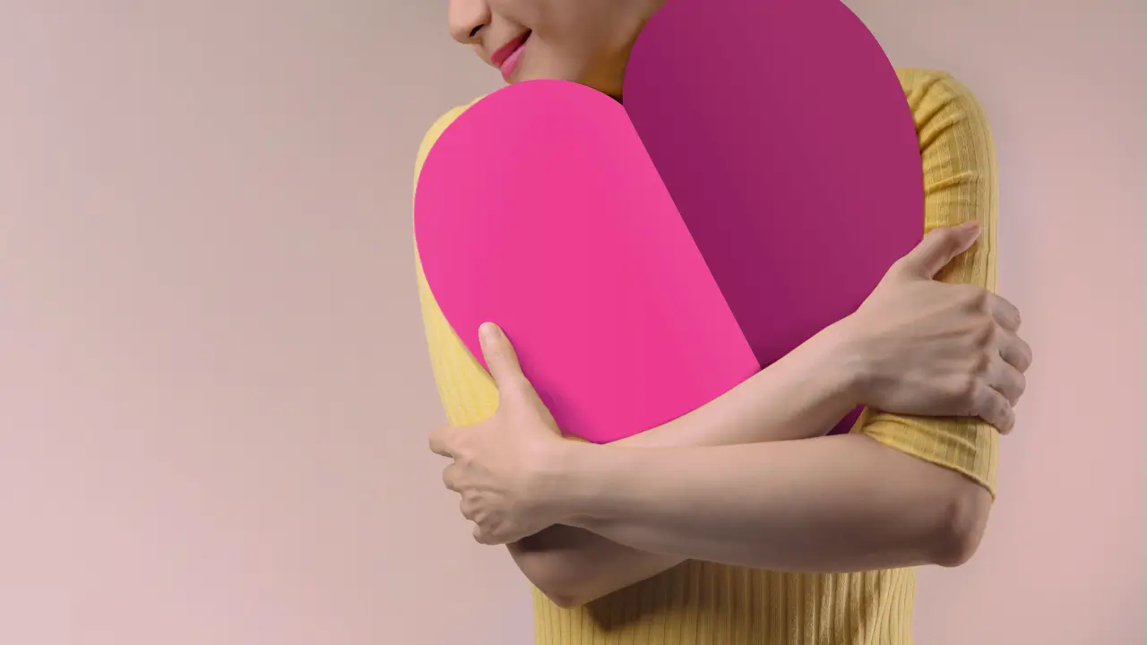 mulher alegre abraçada a um coração simbolizando a autoestima.