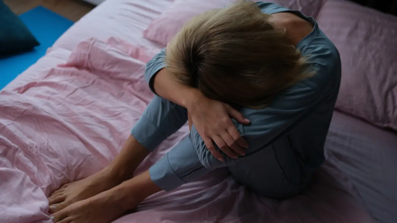 mulher sentada na cama com a cabeça baixa simbolizando culpa.