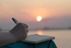 Uma mulher em um ambiente iluminado pelo sol escrevendo para representar Maria Madalena com o diário da graça restauradora