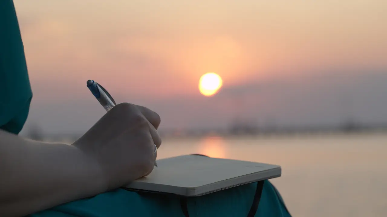 Uma mulher em um ambiente iluminado pelo sol escrevendo para representar Maria Madalena com o diário da graça restauradora