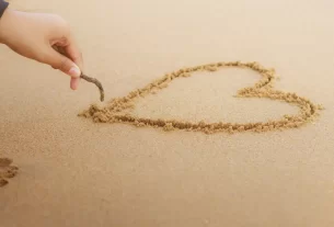 Uma mão desenhando um coração na areia representando o assunto: escolhida para amar.