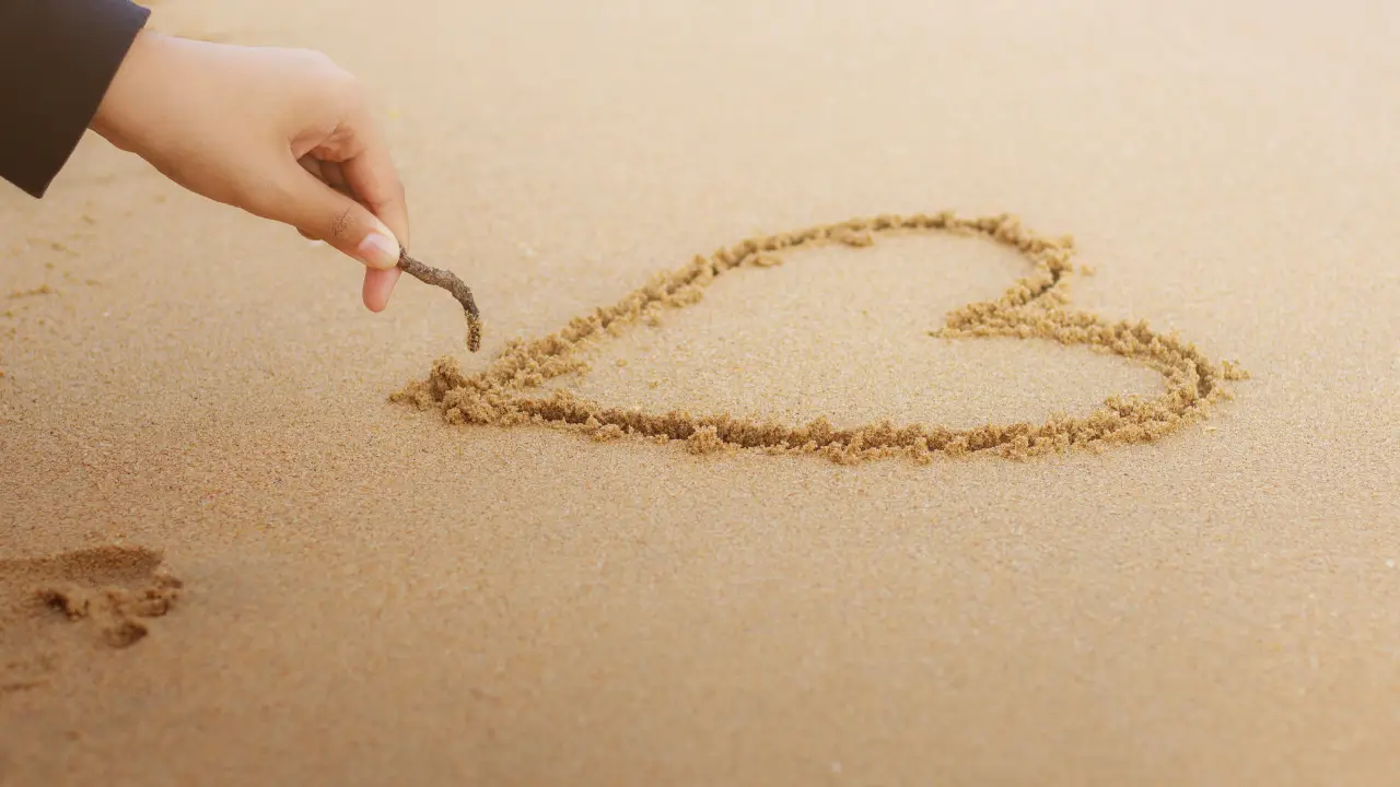 Uma mão desenhando um coração na areia representando o assunto: escolhida para amar.