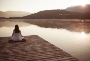Uma mulher sentada no cais à beira de um lago representando a alma cansada que procura descanso em Deus.