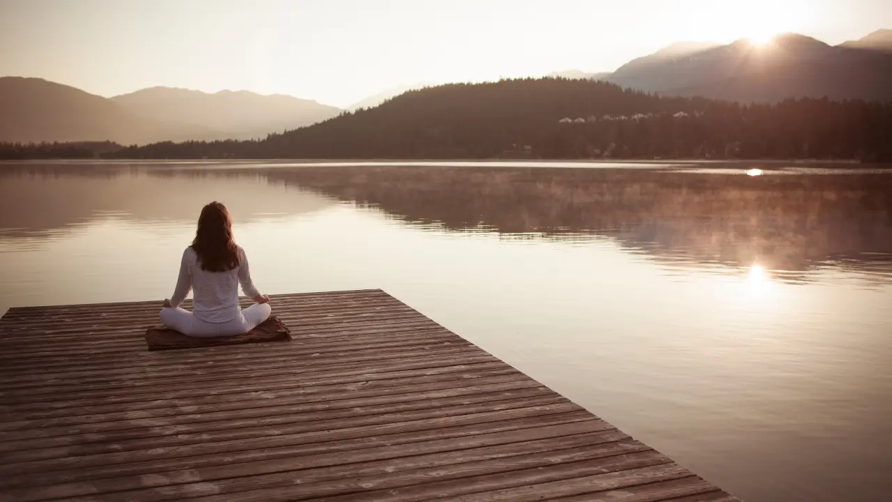 Uma mulher sentada no cais à beira de um lago representando a alma cansada que procura descanso em Deus.