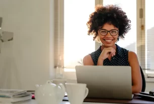 Uma mulher setadaà mesa do trabalho com uma expressão de alegria, simbolizando recomeços no trabalho.