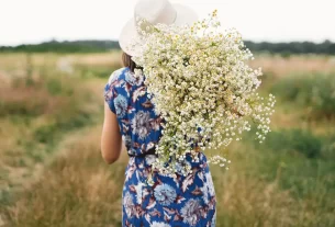 mulher de costas carregando muitas margaridas para simbolizar quem é a mulher aos olhos de Cristo.