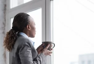 mulher comuma xícara na mão, olhando pela janela para representar a mulher que esconde a dor emocional.