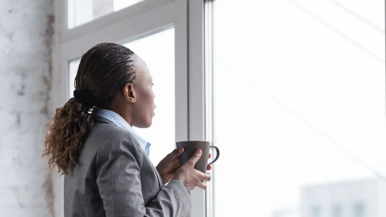mulher comuma xícara na mão, olhando pela janela para representar a mulher que esconde a dor emocional.