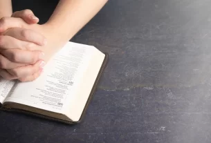 Mãos femininas entrelaçadas sob a Bíblia para simboliza feridas invisíveis e o toque de Deus.