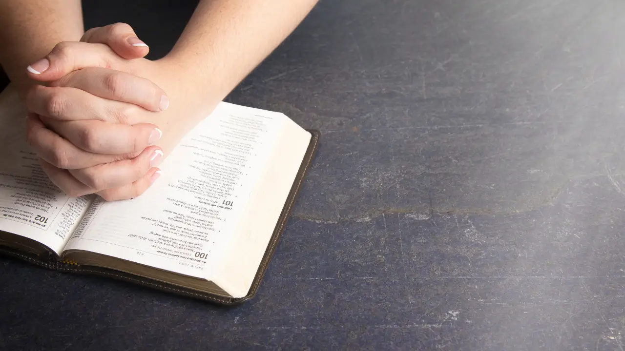 Mãos femininas entrelaçadas sob a Bíblia para simboliza feridas invisíveis e o toque de Deus.