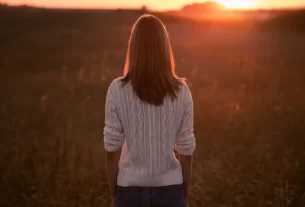 Uma mulher olhando para o horizonte ao nascer do sol, com expressão serena e firmeza no olhar — simbolizando confiança inabalável, esperança e segurança em Deus.