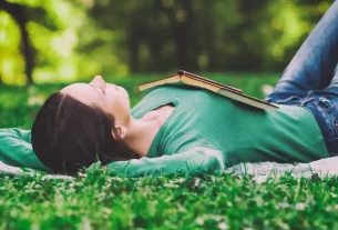 Uma mulher deitada tranquilamente na grma com um livro sobre o colo para simbolizar que descansar é um ato de fé.