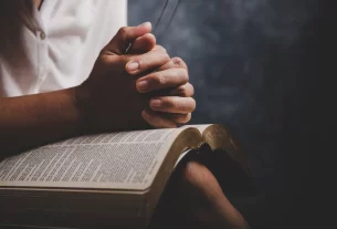 A fé da mulher simbolizada por uma mulher sentada com as mãos entrelaçadas sobre a Bíblia.