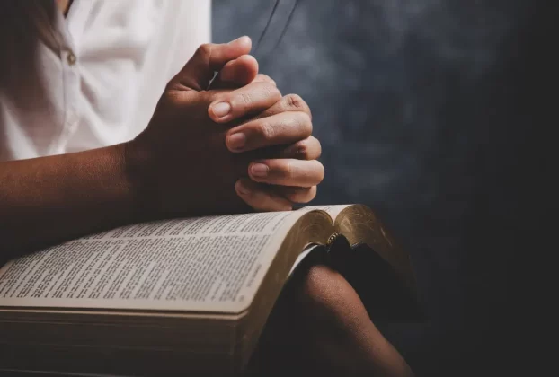 A fé da mulher simbolizada por uma mulher sentada com as mãos entrelaçadas sobre a Bíblia.