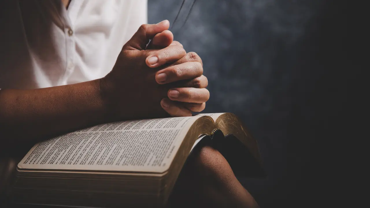 A fé da mulher simbolizada por uma mulher sentada com as mãos entrelaçadas sobre a Bíblia.